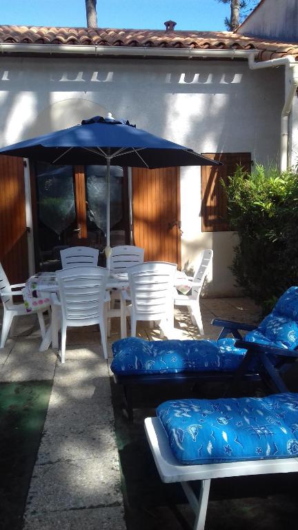 eine Terrasse mit weißen Stühlen und einem blauen Sonnenschirm in der Unterkunft Talaris La Palmyre in Les Mathes