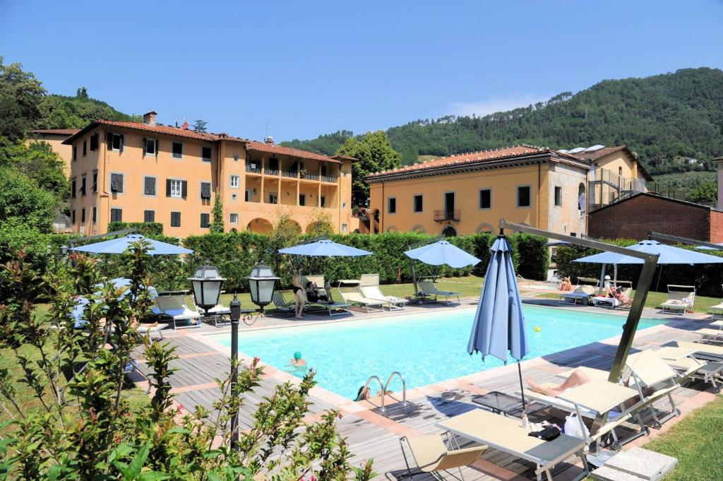 a swimming pool with chairs and umbrellas and buildings at Park Hotel Regina - with air-condition and pool in Bagni di Lucca