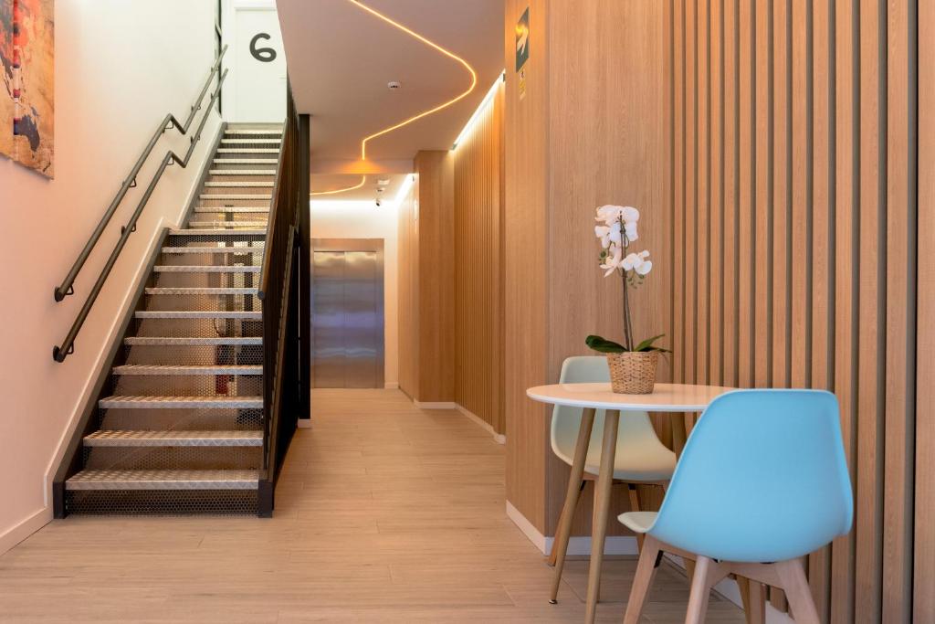 a hallway with stairs and a table and blue chairs at Bilbao ROOMS & KITCHEN Zorroza in Bilbao