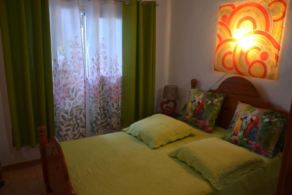 - une chambre avec un lit et une fenêtre avec des rideaux verts dans l'établissement Maison type F3 Chez Jean Michel avec parking Chez Jean Michel, à Sainte-Rose