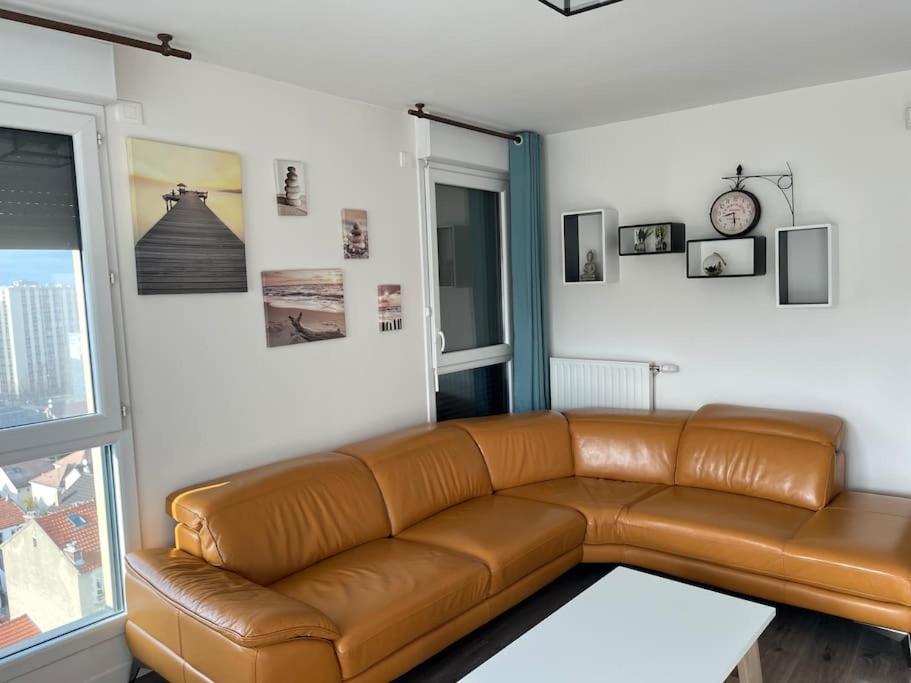 a brown leather couch in a living room with a window at Appartement de Romainville in Romainville