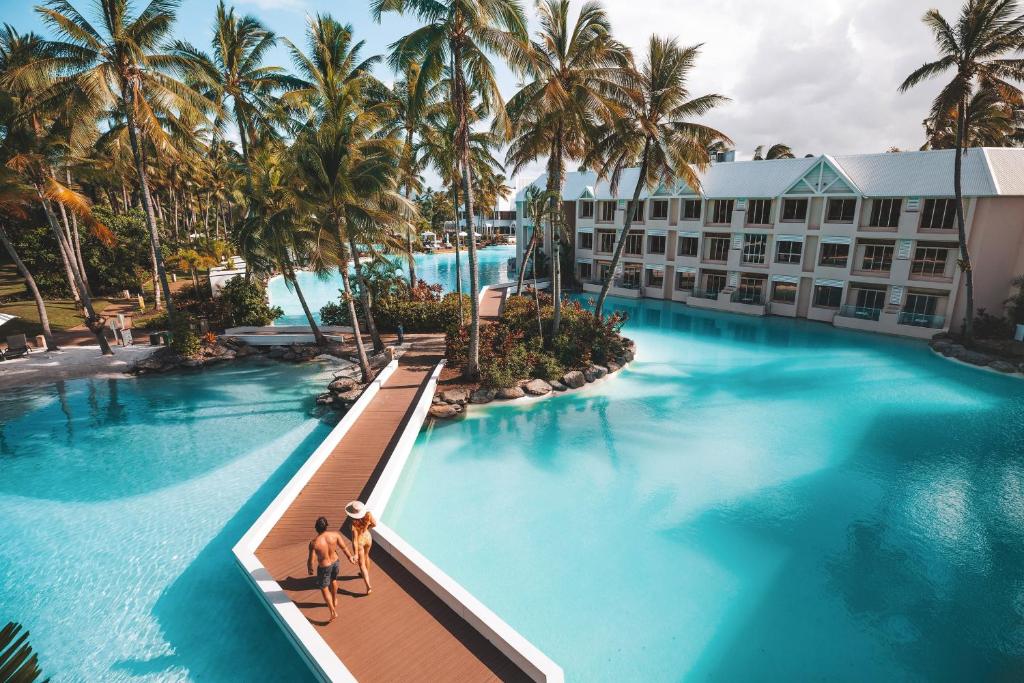 a hotel pool with palm trees and two people sitting on a bridge at Sheraton Grand Mirage Resort, Port Douglas in Port Douglas