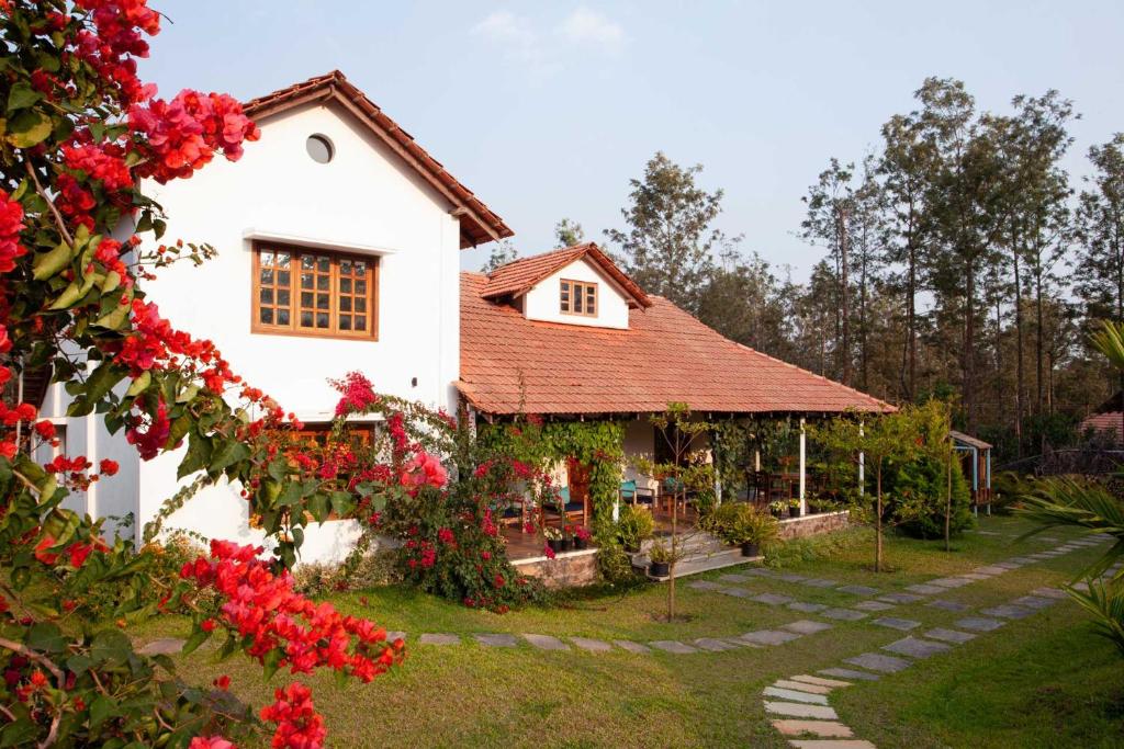 una casa blanca con techo rojo y flores rojas en StayVista at Sienna - Strelitzia 3BHK with Breakfast and Jacuzzi - Luxury Homestay, en Chikmagalur