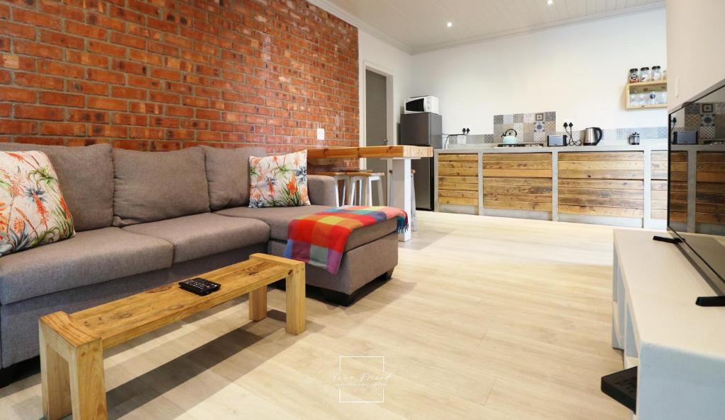 a living room with a couch and a brick wall at Lovely brand new flat near restaurants and beach with solar - free wifi and DSTV in Cape St Francis