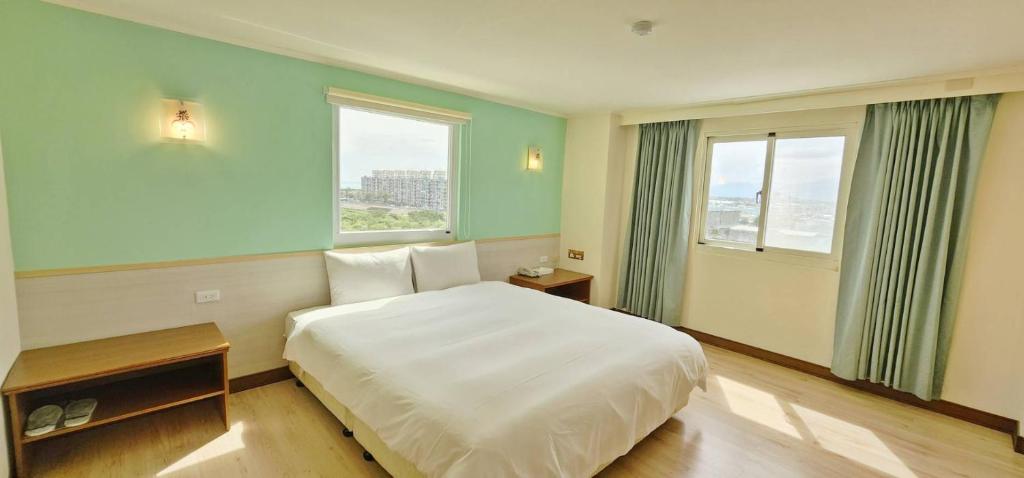 a bedroom with a white bed and two windows at Apple Hotel in Taitung City