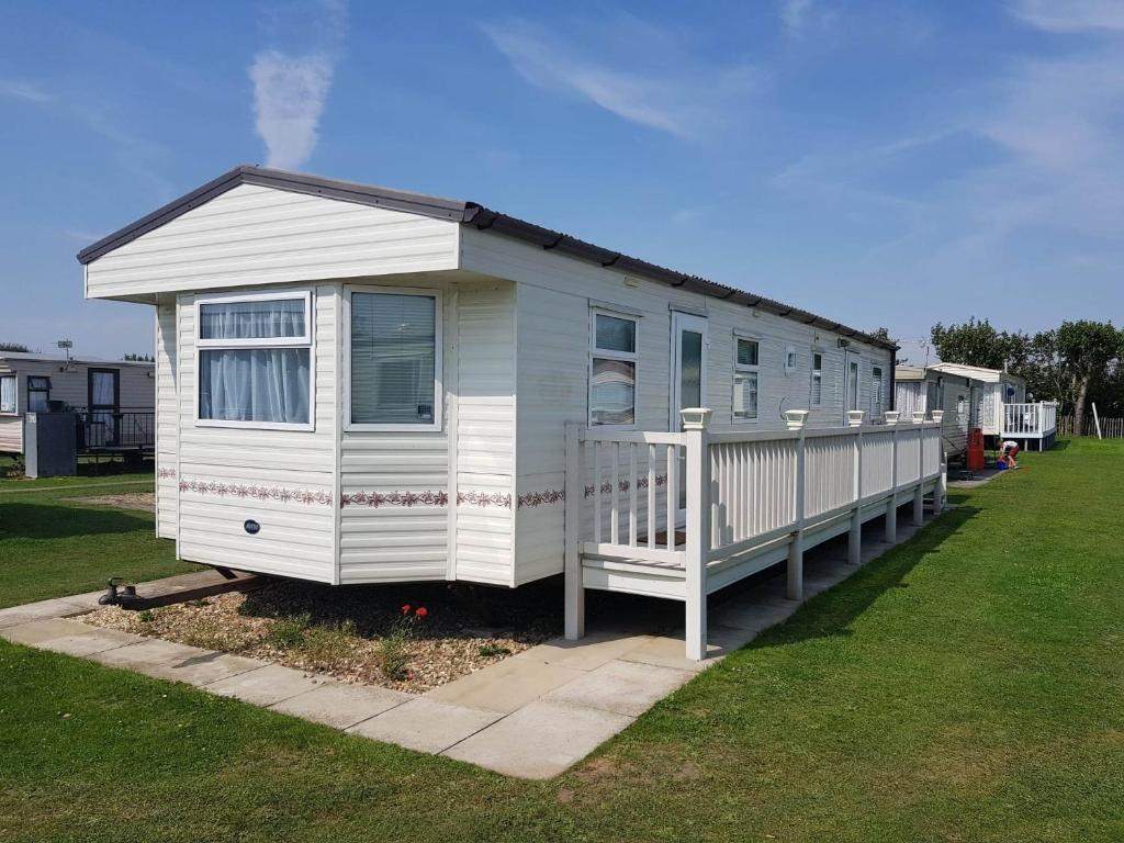 a small white house with a porch in a yard at S295 3 BED DELUXE PET FRIENDLY CARAVAN in Chapel Saint Leonards