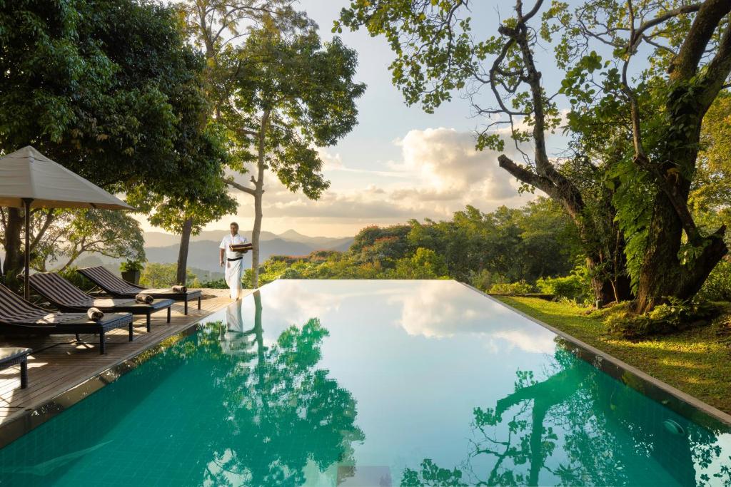 un homme debout à côté d'une piscine bordée d'arbres dans l'établissement Mountbatten Bungalow- Thema Collection, à Kandy