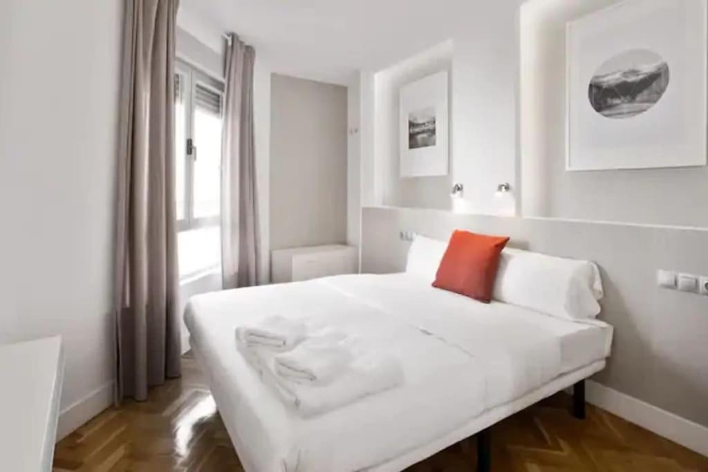 a white bedroom with a white bed with a red pillow at Apar. renovado en Leganitos (Gran Vía) con portero in Madrid