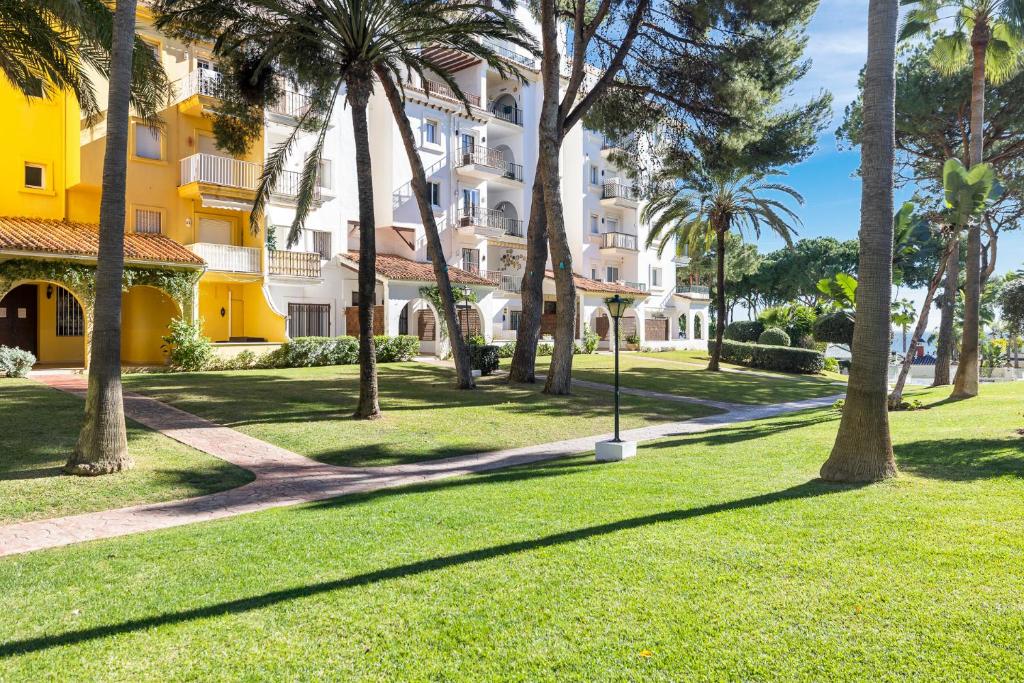 park z palmami i żółtym budynkiem w obiekcie Luminoso apartamento en Andalucía del Mar w Marbelli