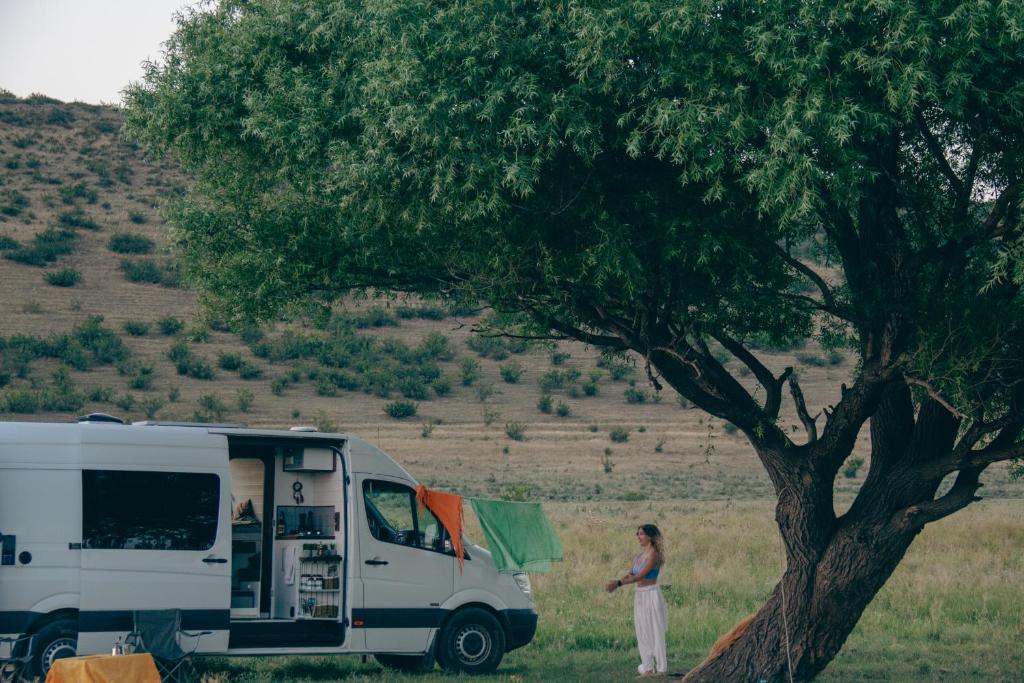 una mujer de pie junto a una caravana junto a un árbol en Geo Campers - Full time living camper rental in Kutaisi, Tbilisi, Batumi, Georgia, en Kutaisi