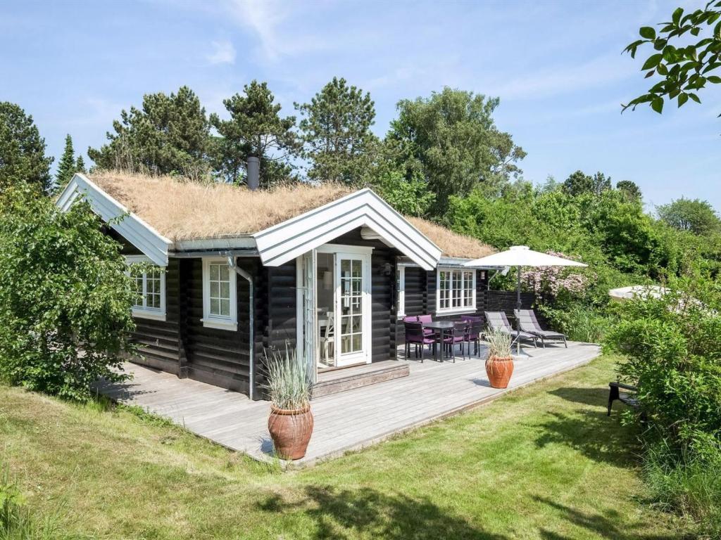 uma cabana de madeira com um telhado de palha e um deque em Holiday Home Ottil - 1km from the sea in Sealand by Interhome em Tisvildeleje
