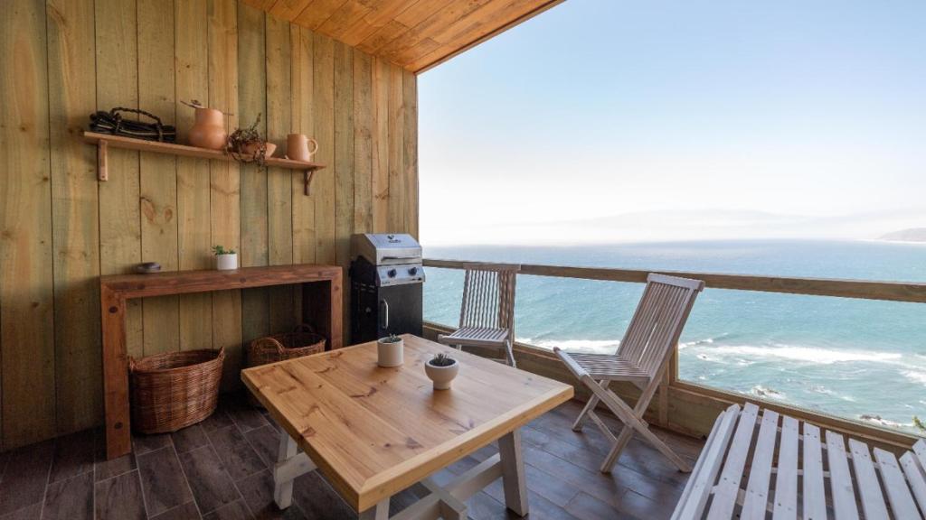 un porche de madera con mesa, sillas y el océano en Hotel Puerto Viejo Llico, en Llico