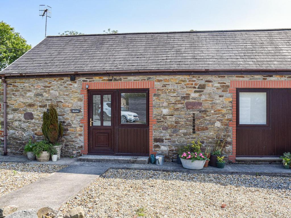 uma casa de pedra com uma porta, janelas e plantas em Meadow Cottage em Gowerton