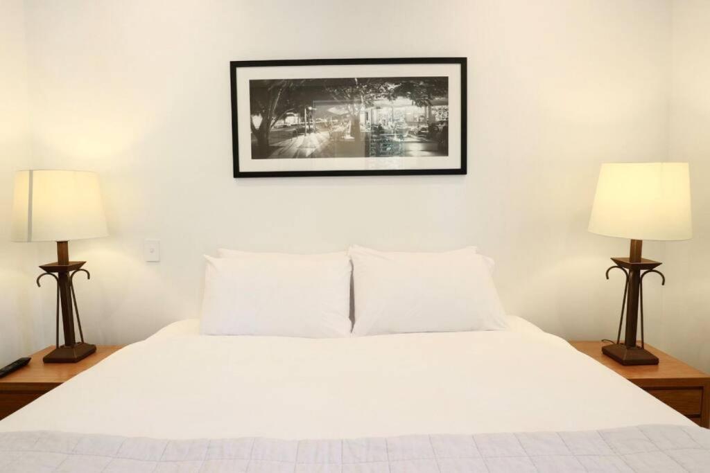 a bedroom with a white bed with two lamps at 617 Hastings Street metres to the beach in Noosa Heads