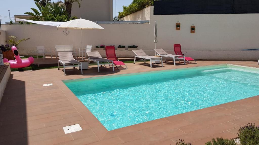 a swimming pool with chairs and a table and an umbrella at VILLA HERAIA in Marina di Ragusa