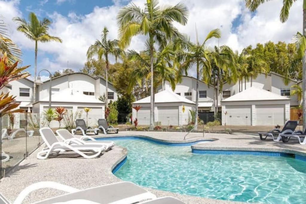 努薩維爾的住宿－14 Gorgeous Waterfront Noosa Oasis，一座房子前面的游泳池,里面设有椅子和棕榈树