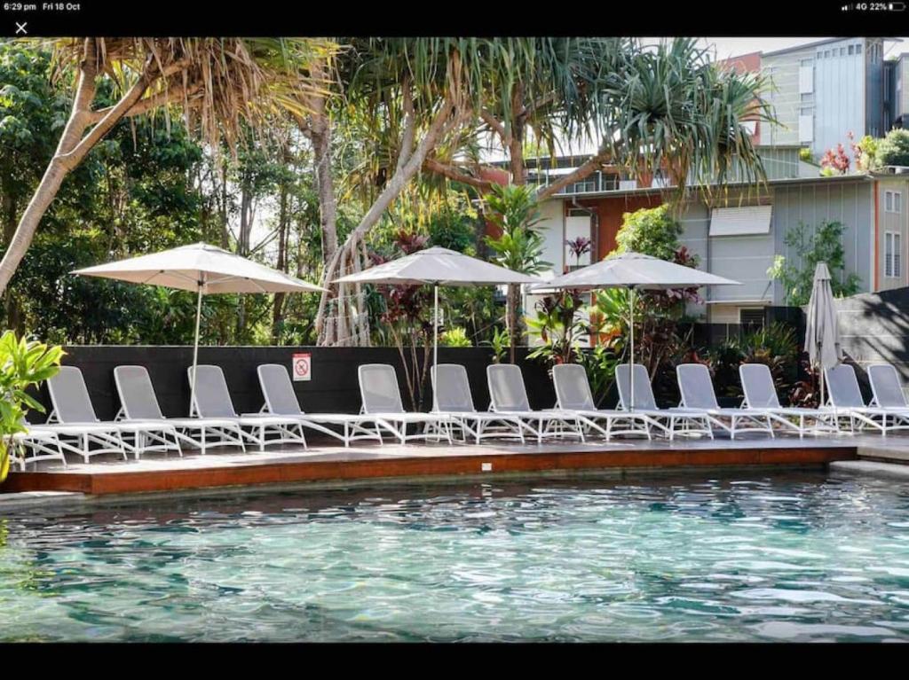 eine Gruppe von Stühlen und Sonnenschirmen neben einem Pool in der Unterkunft 7211 Lovely 2 Bedroom Viridian Noosa in Noosa Heads