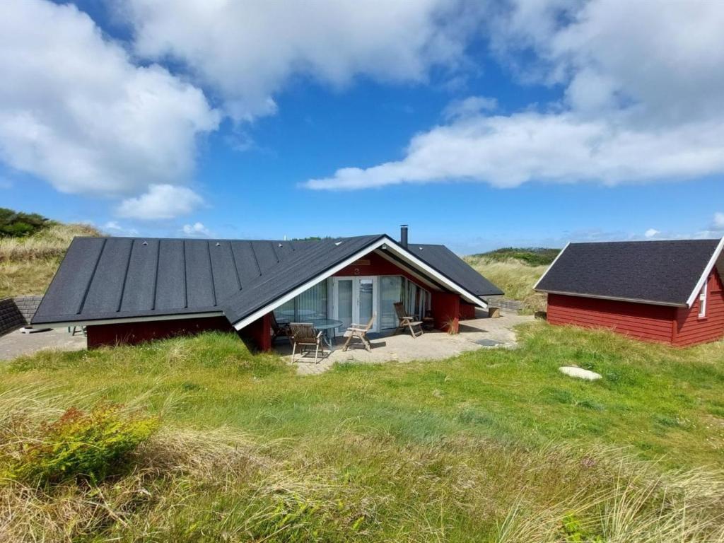 uma casa vermelha com um telhado preto num campo em Holiday Home Beneta - 300m from the sea in Western Jutland by Interhome em Hvide Sande