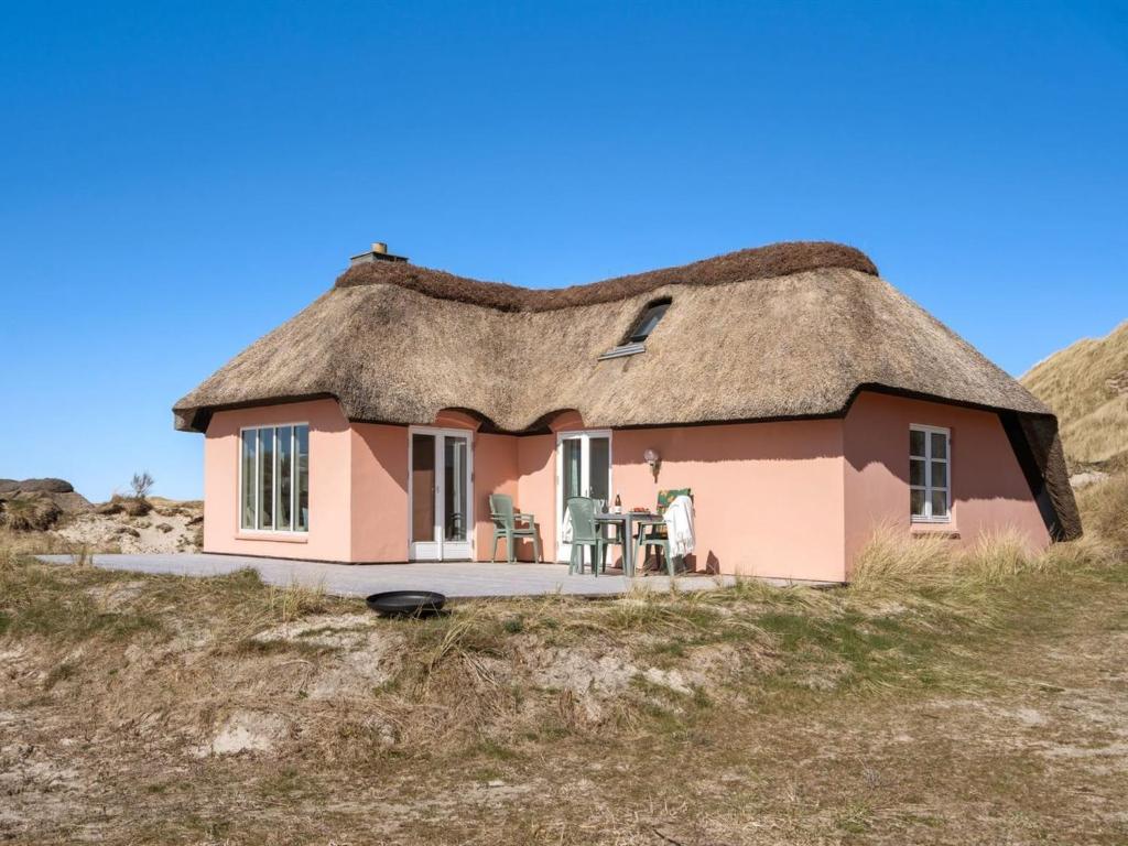 ein kleines rosafarbenes Haus mit einem Strohdach auf einem Hügel in der Unterkunft Holiday Home Tabea - 150m from the sea in NW Jutland by Interhome in Løkken