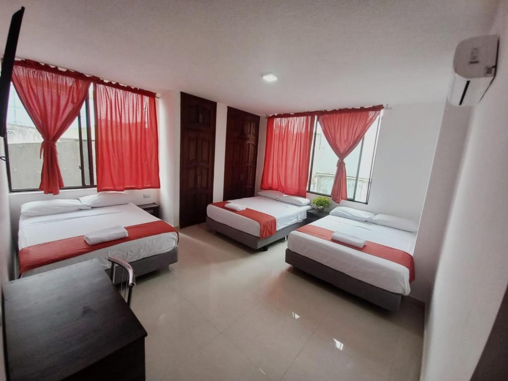 two beds in a room with red curtains and windows at HOTEL DIAMANTE in Santo Domingo de los Colorados