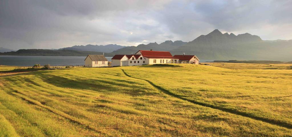 a house on top of a grassy field with mountains in the background at Berunes HI Hostel in Berunes