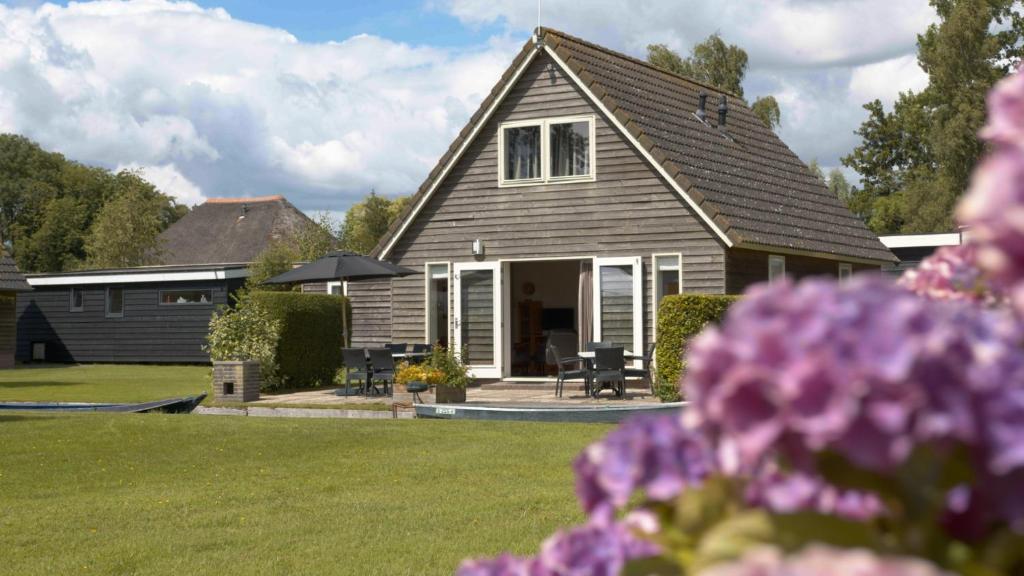 une maison avec une cour ornée de fleurs violettes dans l'établissement De Sloothaak, à Giethoorn