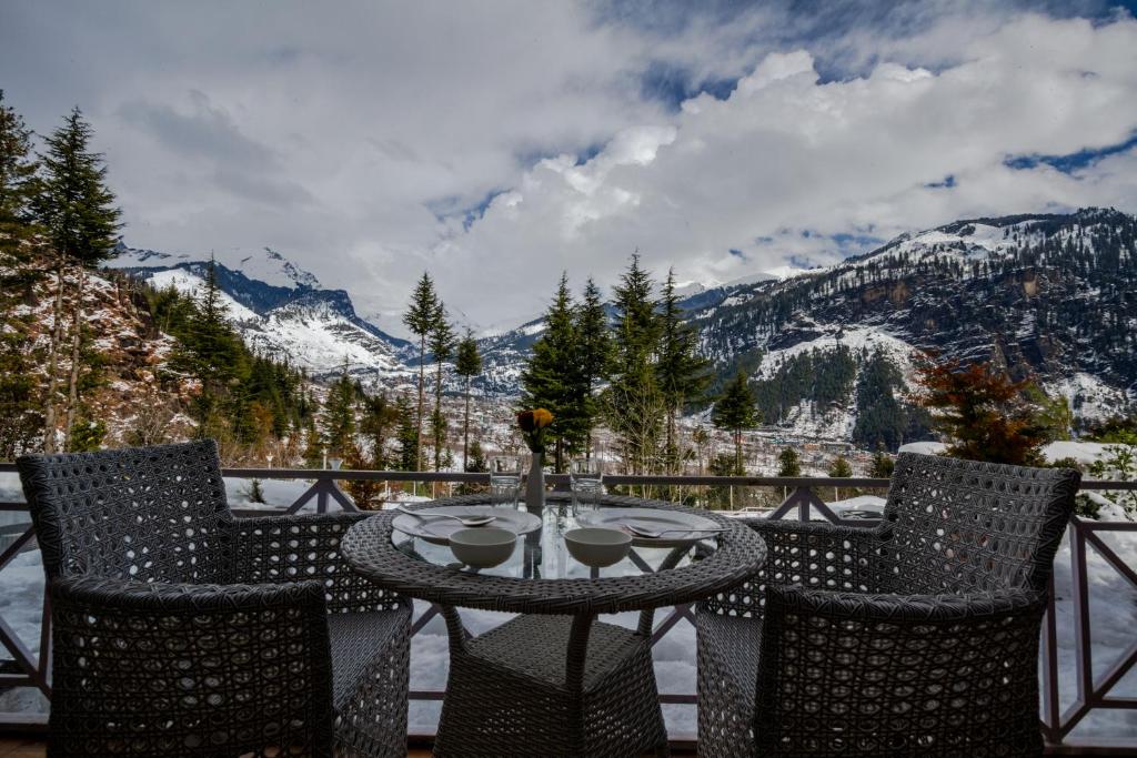 a table and chairs on a balcony with mountains at Baan by Snow City Farm in Vashisht