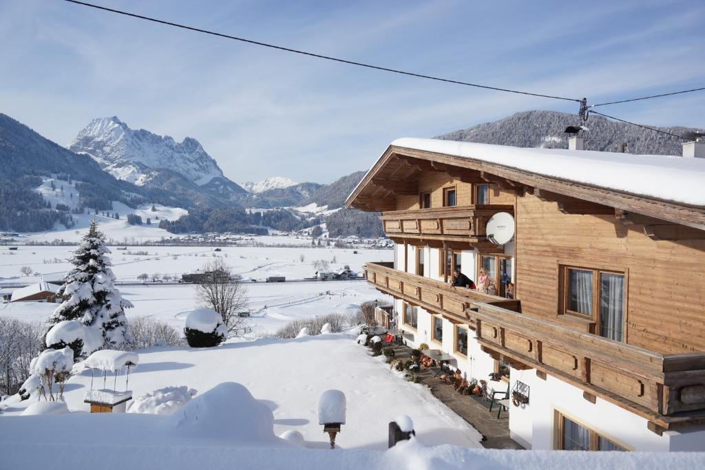 un edificio de madera en la nieve con montañas en el fondo en Pension Sonnleit'n, en Kirchdorf in Tirol