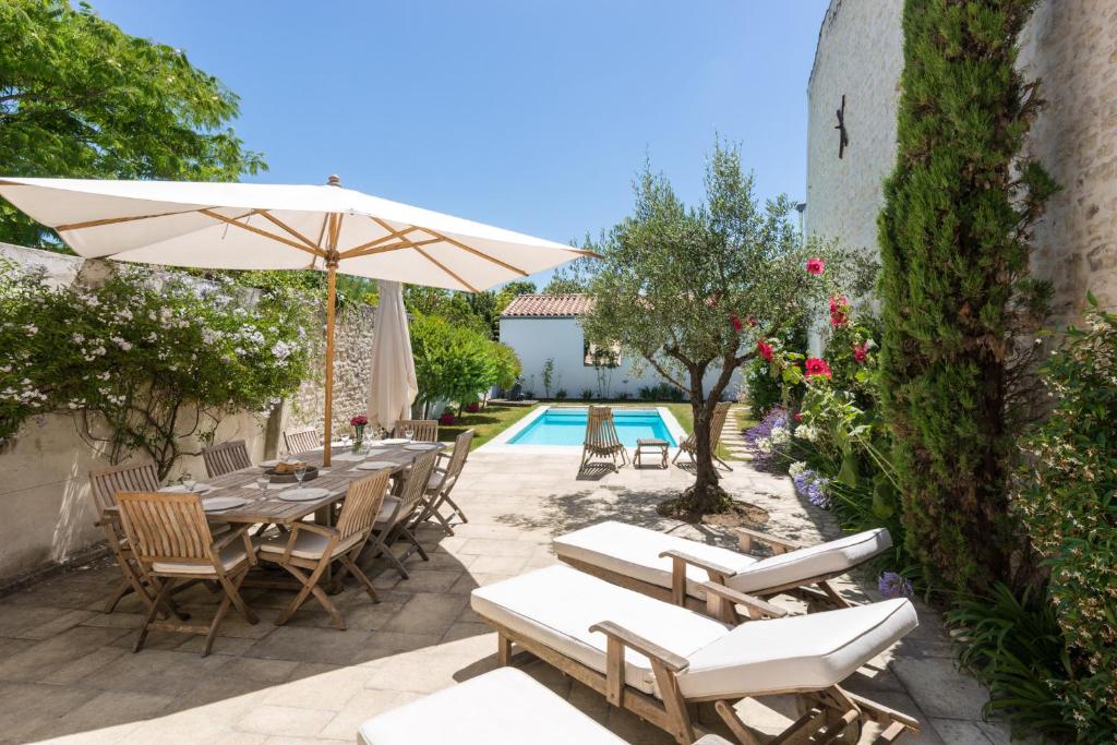 eine Terrasse mit einem Tisch, Stühlen und einem Sonnenschirm in der Unterkunft Villa Petit Sergent in Le Bois-Plage-en-Ré