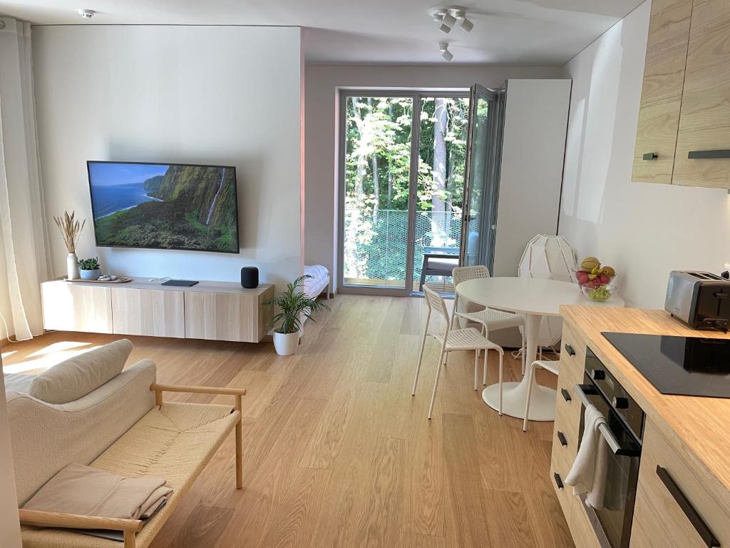 a kitchen and living room with a table and a tv at Sunny apartment with forest view in Juodkrantė