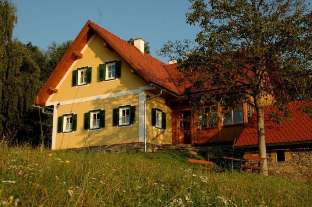 una casa gialla con tetto rosso su un campo di Ferienwohnung Stiegelbauer Fichte a Sausal