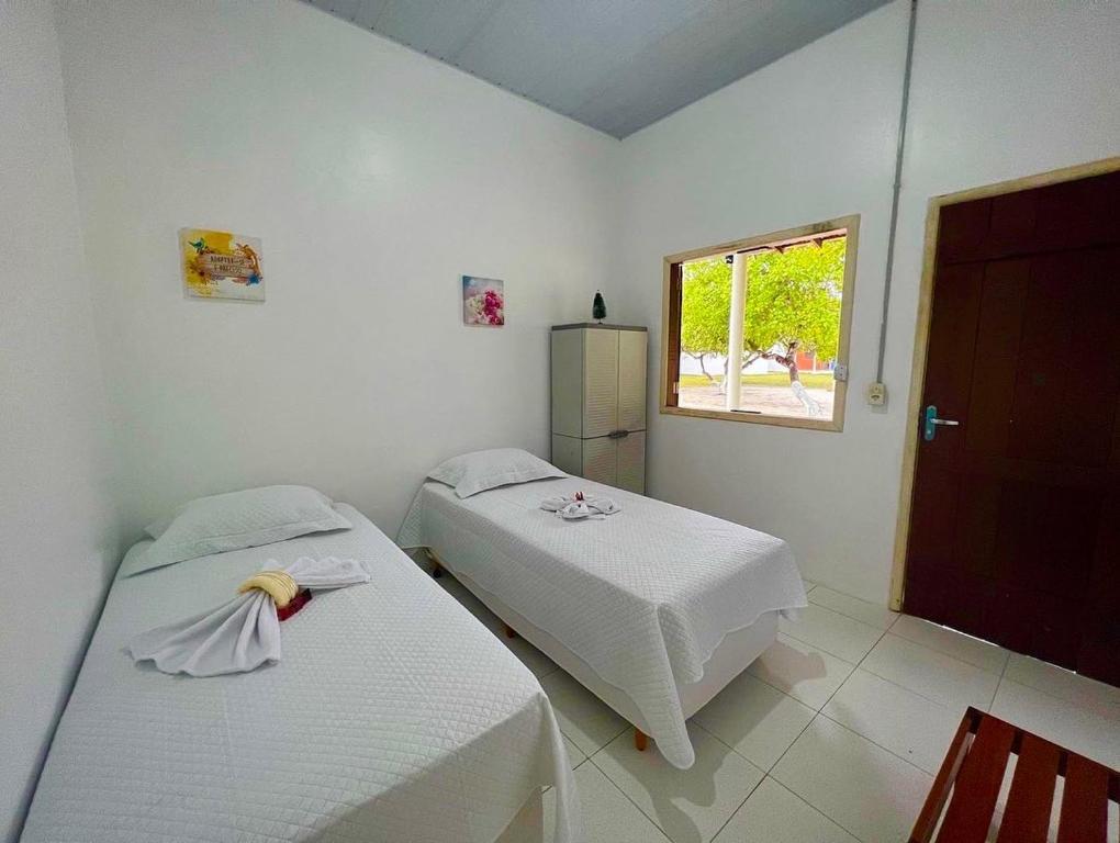 two beds in a white room with a window at POUSADA ESTRELA DA MANHÃ in Barreirinhas