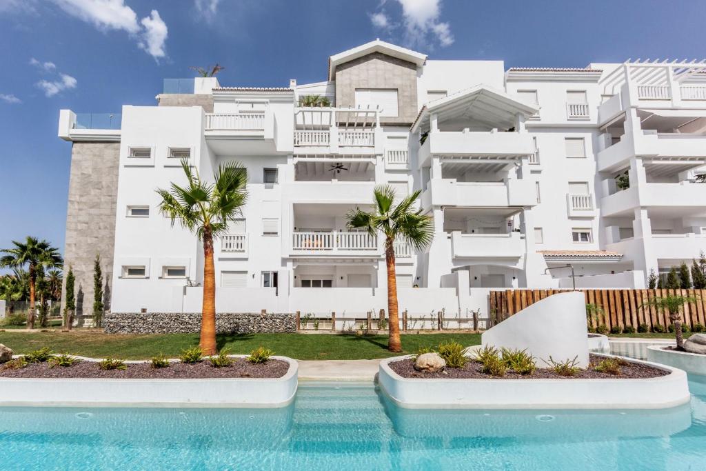 duży biały budynek z palmami przed basenem w obiekcie Homity Exclusive Playa Granada Beach & Golf - Marina Golf w mieście Motril