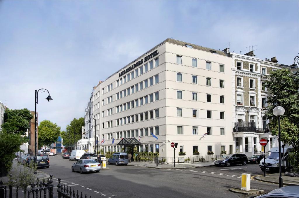 un grand bâtiment blanc avec des voitures garées devant lui dans l'établissement Ambassadors Hotel, à Londres
