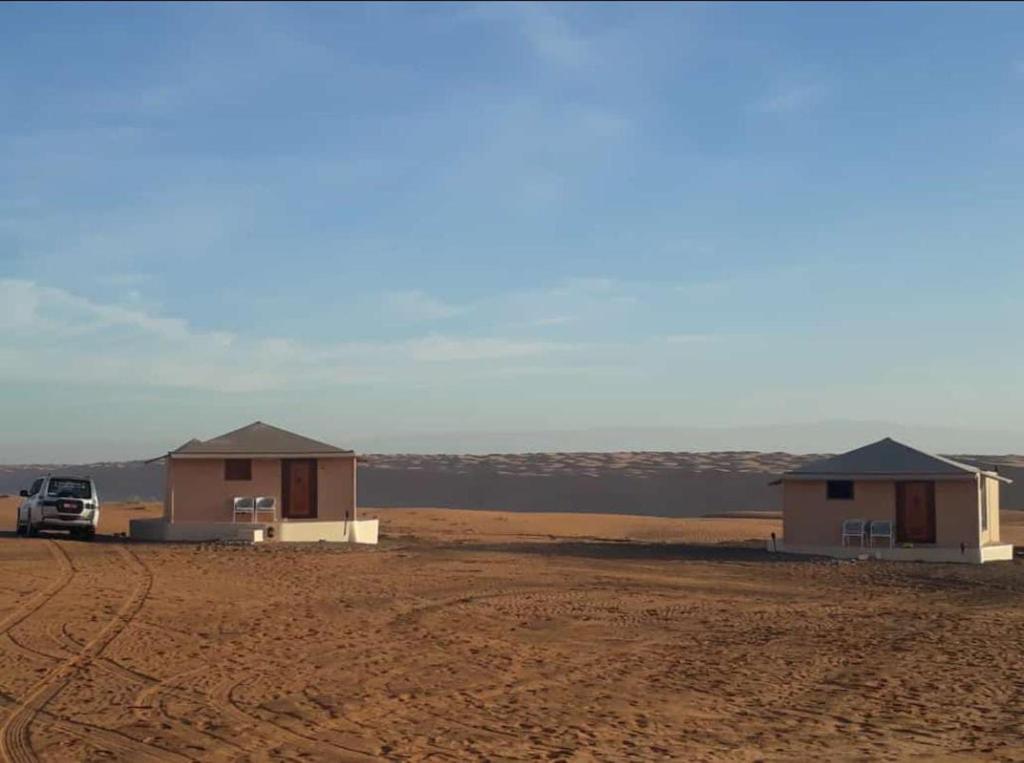Deux maisons dans le désert avec un camion garé à côté d'elles dans l'établissement Safari Dunes Camp, à Ḩawīyah