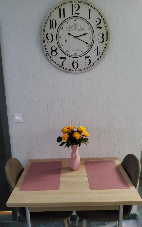 een tafel met een vaas met bloemen en een klok aan de muur bij Brodovskiy- Apartment in Neckarsulm