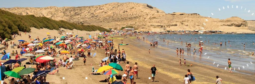 a crowd of people on a beach with umbrellas at Veredas al sol puerto piramides in Puerto Pirámides