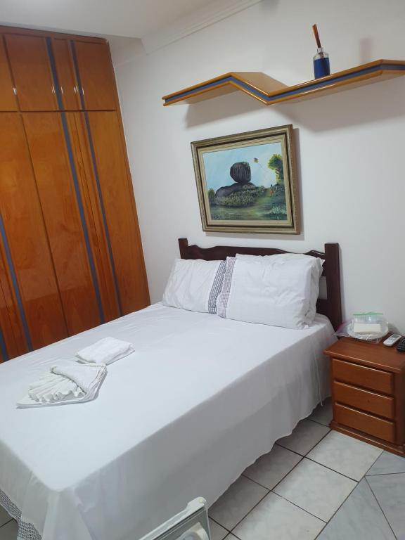 um quarto com uma cama branca e um armário de madeira em SUÍTE Alfa em Vila Velha