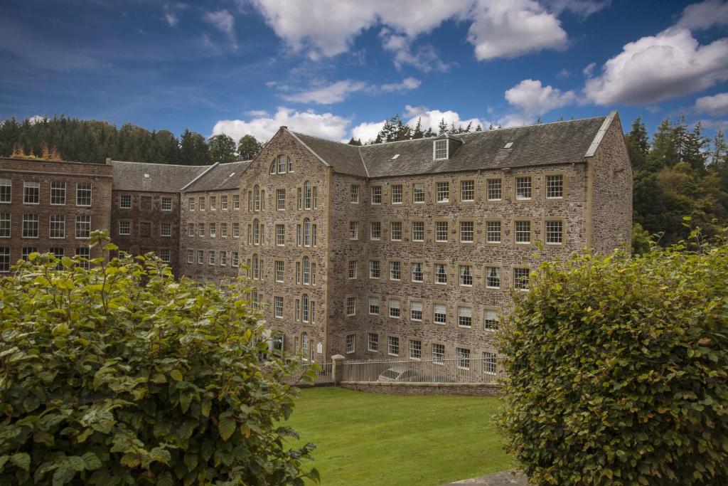 ein großes Backsteingebäude mit grünem Rasen davor in der Unterkunft New Lanark Mill Hotel in Lanark