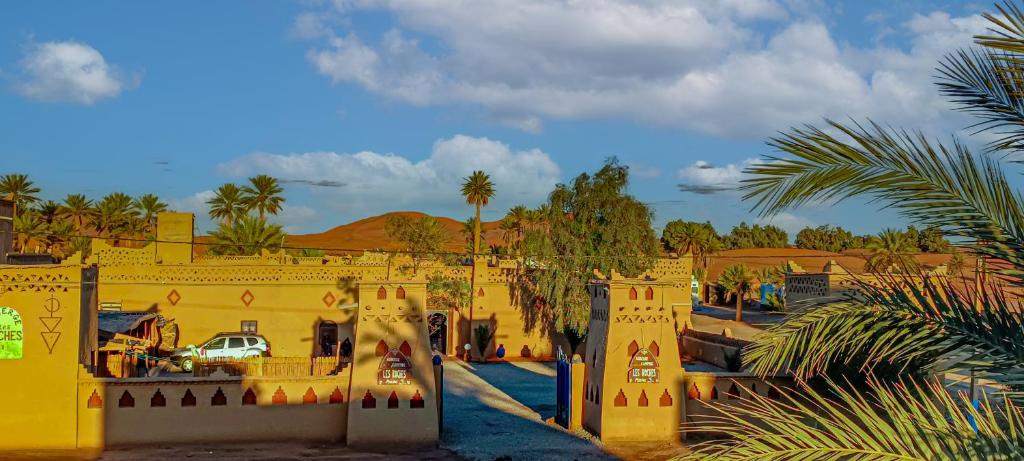 ein gelbes Gebäude mit Palmen und Bergen im Hintergrund in der Unterkunft Auberge Les Roches in Merzouga