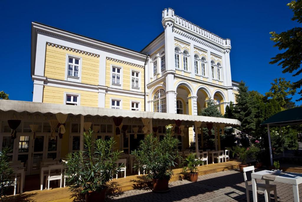 een groot geel en wit gebouw met bomen voor de deur bij Hotel Astoria in Balatonfüred
