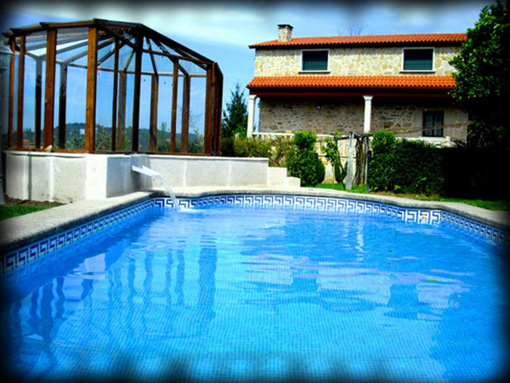 una grande piscina blu di fronte a una casa di Casa Rural Os Carballos a Pontevedra