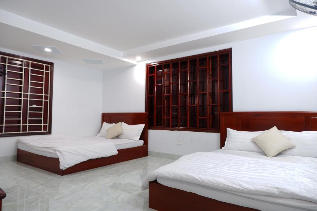 two beds in a room with white walls and windows at Thinh Khang Guesthouse in Buon Ma Thuot