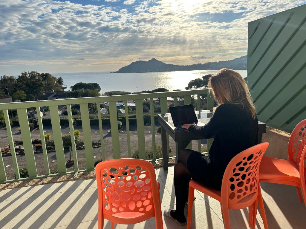 une femme assise à une table avec un ordinateur portable sur un balcon dans l'établissement Front de mer, vue exceptionnelle panoramique, à Agay