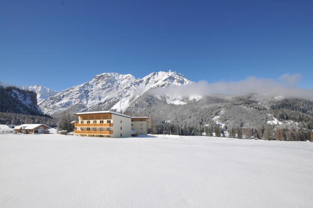 a building on a snow covered field with a mountain at Hotel Asterbel in Braies