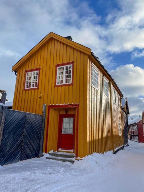 una casa amarilla con una puerta roja en la nieve en Villa Gulstua en Røros
