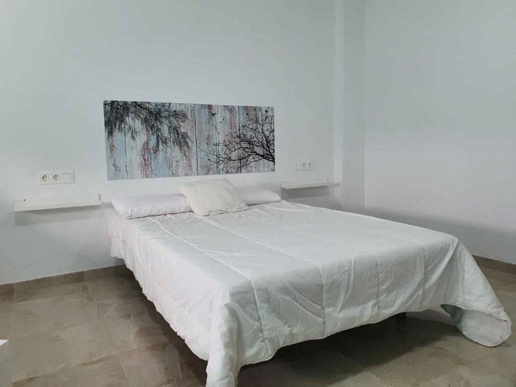 un letto in una camera bianca con un dipinto sul muro di Apartamento Rompeolas a Mazagón