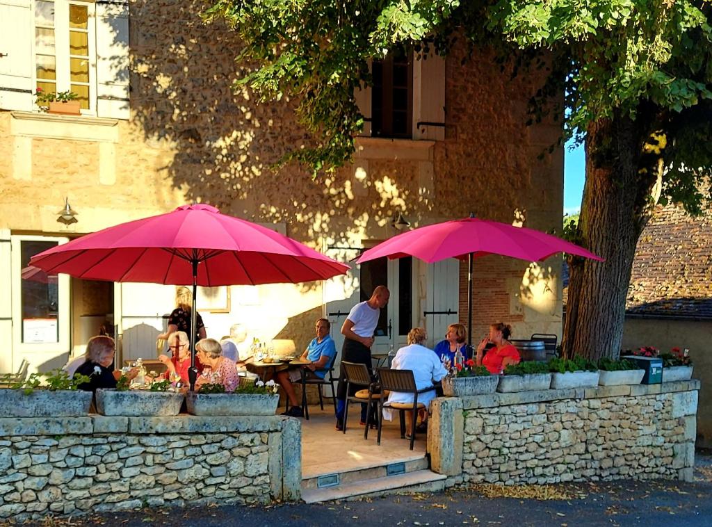un groupe de personnes assises à une table sous des parapluies roses dans l'établissement Les Cèdres, à Saint-Marcel-du-Périgord