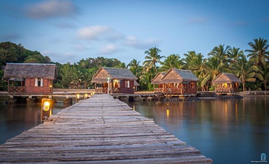 un puente de madera sobre un cuerpo de agua con casas en Lakana Hotel en Isla Santa María