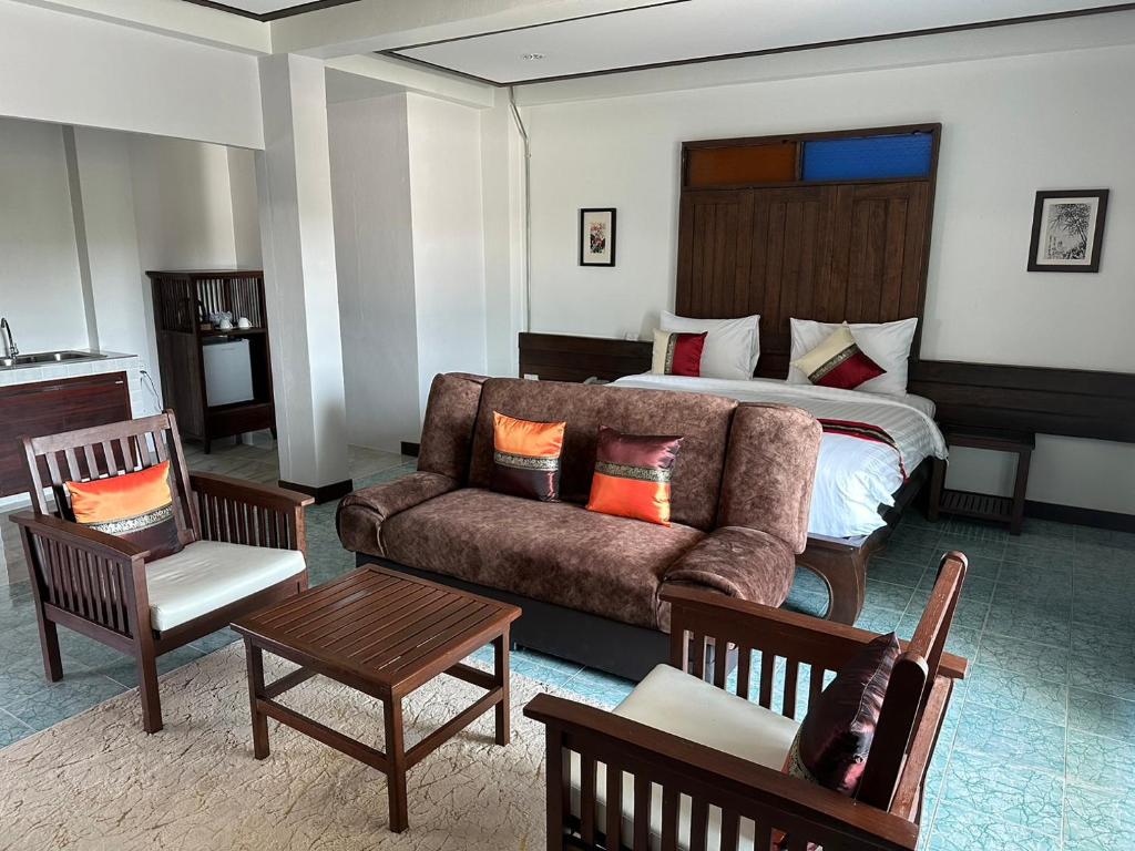 A compact open-plan room with a double bed, sofa, armchairs and a kitchenette edge.